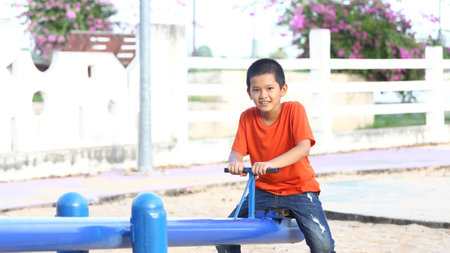 A cheerful child enjoys a sunny day at the playground, playing on a blue seesaw. This vibrant scene captures the essence of childhood joy and outdoor fun.の写真素材