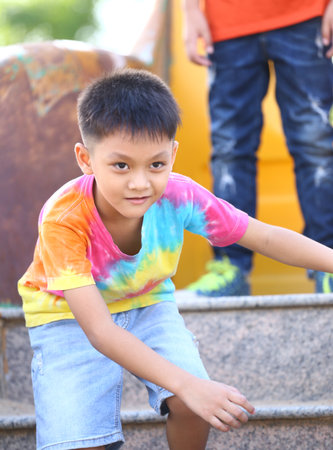 A young boy wearing a bright tie-dye shirt plays joyfully on outdoor stairs, showcasing his playful spirit and vibrant energy in a sunny environment.の写真素材