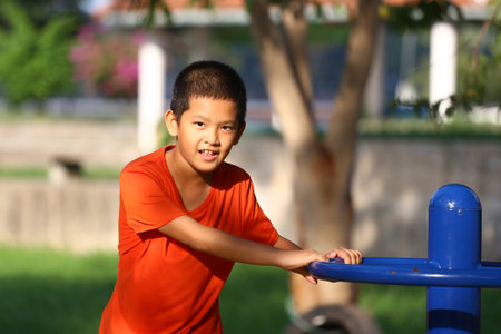 A cheerful young boy in a bright orange shirt enjoys his time at the playground, showcasing his vibrant personality and love for outdoor play.の写真素材