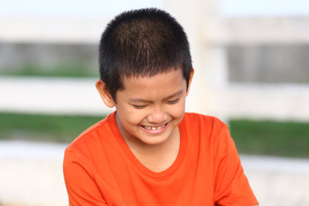 A young boy with a bright smile enjoys a moment of joy while wearing an orange shirt. His cheerful expression captures the essence of childhood happiness in a sunny outdoor setting.の写真素材