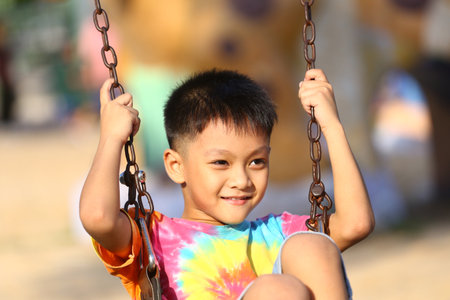 A cheerful child smiles while playing on a swing in a vibrant, colorful t-shirt. This joyful moment captures the essence of childhood fun and freedom.の写真素材
