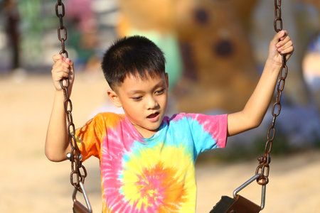 A joyful child swings at a playground, showcasing vibrant colors in their outfit. This image captures the essence of childhood joy and carefree playfulness.の写真素材