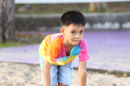 A young boy in a colorful tie-dye shirt enjoys playing outdoors in a park. His joyful expression captures the essence of childhood and exploration.の写真素材