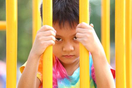 A young child peers through yellow playground bars, showcasing a range of emotions. The vibrant colors highlight the playful atmosphere of childhood.の写真素材