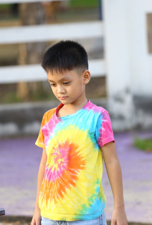 A young boy wearing a colorful tie-dye t-shirt enjoys playing outdoors. The vibrant colors stand out against a natural background, capturing a moment of innocence and joy.の写真素材