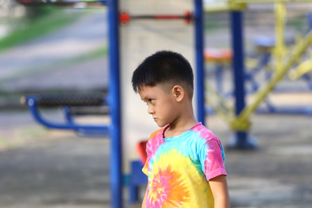 A young boy in a colorful tie-dye shirt stands thoughtfully in a playground, capturing the essence of childhood innocence and outdoor fun.の写真素材
