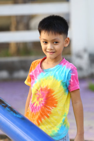 A cheerful boy wearing a vibrant tie-dye shirt enjoys a moment outdoors at the playground, embodying the essence of childhood joy and carefree spirit.の写真素材