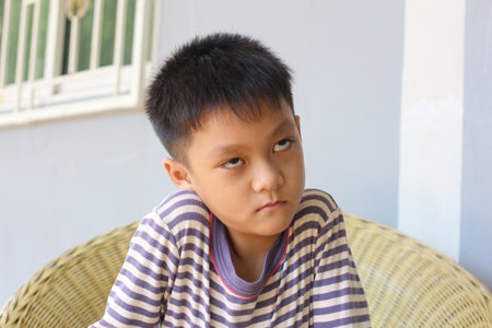 A thoughtful boy sitting calmly on a chair, displaying a contemplative expression. The scene captures youthful innocence and tranquility in a casual indoor setting.の写真素材