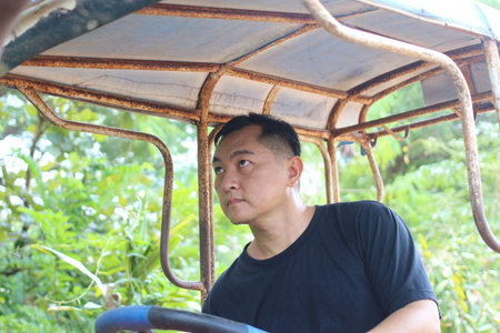 A man is focused on driving a vehicle in a lush outdoor environment, showcasing dedication and hard work amidst greenery and rural scenery.の写真素材