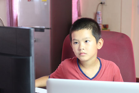 A young boy engages with a computer screen in a home environment, showcasing focus and concentration while learning or completing homework tasks.の写真素材