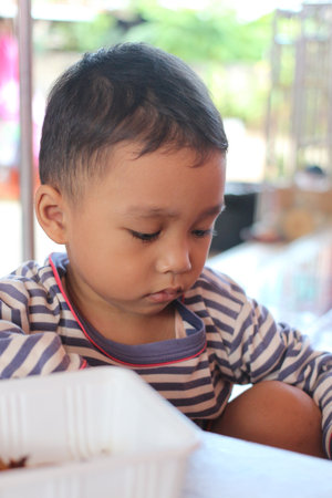 A young boy in a striped shirt sits quietly, lost in thought while engaging in playtime. His concentration and gentle expression capture the essence of childhood innocence.の写真素材
