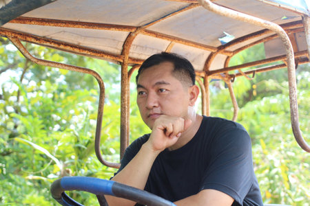 A thoughtful man sits in a rustic vehicle, surrounded by vibrant greenery. He appears pensive, enjoying the serene moment in nature.の写真素材