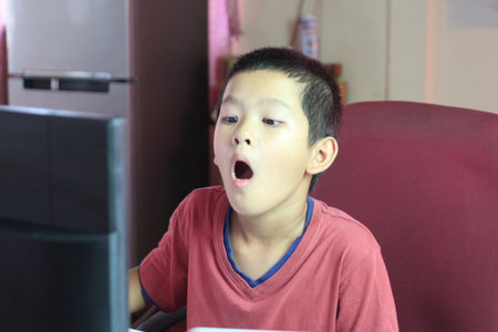 A young boy displays a surprised expression while using a computer at home. His engagement with technology highlights curiosity and excitement in a casual setting.の写真素材