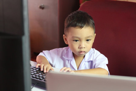 A young child sits at a desk, focused on a computer screen, showcasing early engagement with technology in a playful learning environment.の写真素材