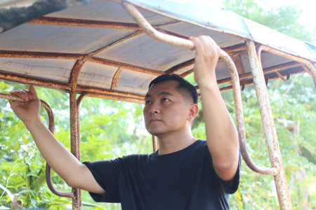A man standing in a vintage vehicle, gripping metal bars with a contemplative expression. Surrounded by lush greenery, he embodies exploration and adventure.の写真素材