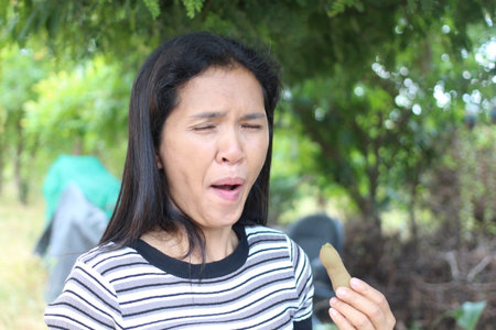 A young woman experiences a delightful moment outdoors while enjoying a snack. Her expression captures the joy and surprise of tasting something fresh in a natural setting.の写真素材