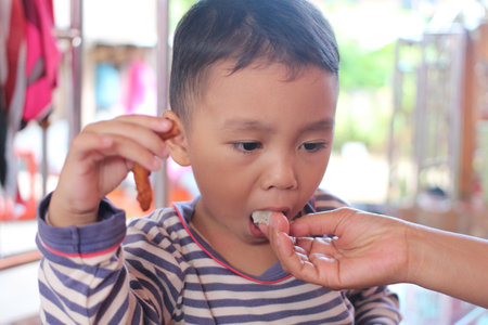 A young child experiences joy while receiving a snack from a caring adult. This moment captures the warmth of family bonding during mealtime.の写真素材