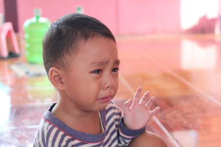 A young child expresses deep emotion as he cries in a cozy indoor setting with pink walls. The image captures a poignant moment of vulnerability and innocence.の写真素材