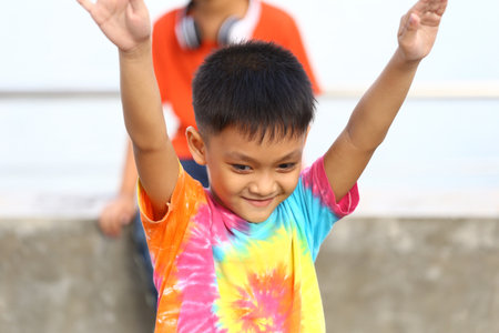 A joyful child wearing a colorful tie-dye shirt celebrates with outstretched arms, embodying...