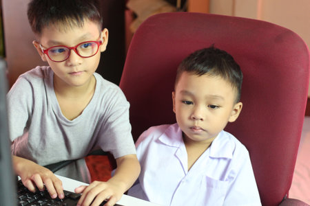 Two children are engaged with a computer, showcasing a moment of learning and interaction in a cozy indoor environment. Their expressions suggest curiosity and focus.の写真素材