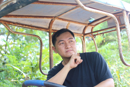 A thoughtful man sits in an old tractor, surrounded by lush greenery. The perfect blend of tranquility and rural charm, ideal for agricultural themes.の写真素材