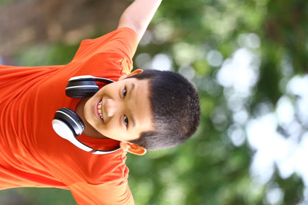 A cheerful boy wearing headphones enjoys a sunny day outdoors, expressing joy and freedom while engaging in playful activities surrounded by nature.の写真素材