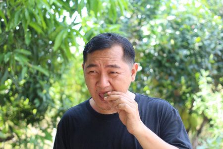 A man enjoys a bite of food while surrounded by lush greenery, capturing a moment of peace and connection with nature in a bright, sunlit setting.の写真素材