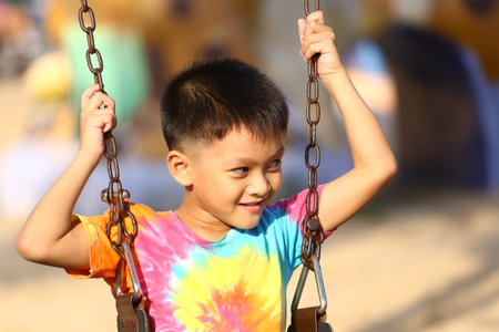 A joyful child swings with a big smile, wearing a colorful tie-dye shirt. This lively scene captures the essence of childhood joy and outdoor fun.の写真素材