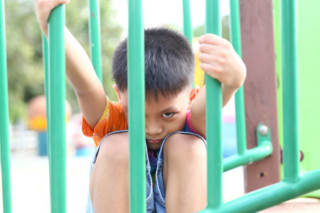 A young boy is captured sitting in a playground, showcasing a vibrant expression of curiosity and playfulness. The bright setting adds to the joyful atmosphere.の写真素材