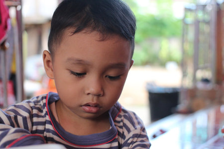 A thoughtful young child is engrossed in a task, showcasing innocence and curiosity in a serene setting. Perfect for themes on childhood and education.の写真素材