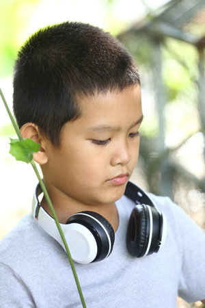 A young boy enjoys listening to music with headphones in a serene outdoor setting. His thoughtful...