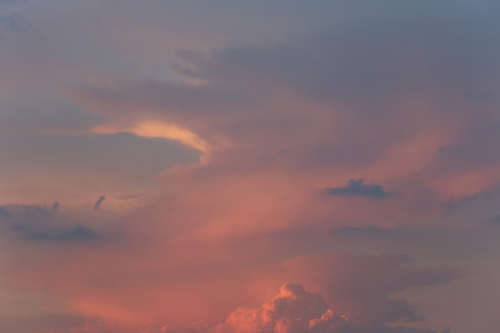 Stunning sky filled with soft pink and lavender clouds illuminated by golden light at sunset,...
