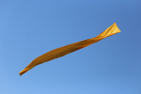 A stunning golden fabric dances in the wind against a backdrop of a clear blue sky, embodying vibrancy and freedom, ideal for creative and artistic projects.の写真素材
