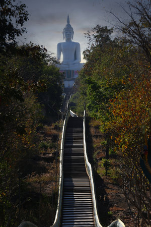 Staircase leads up to the temple at the top of the mountain, and behind it there is a large white Buddha statue.の写真素材