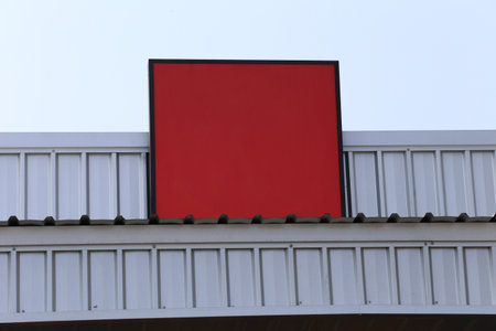 A vibrant blank red sign mounted on a modern building stands out against a clear blue sky, offering...