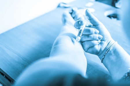 Woman puts a syringe in the arm with medicineの写真素材