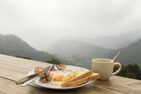 breakfast and coffee cup on wooden table with nature mountain backgroundの写真素材