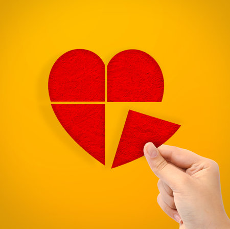 Hand holding cut out heart paper shape on yellow backgroundの写真素材