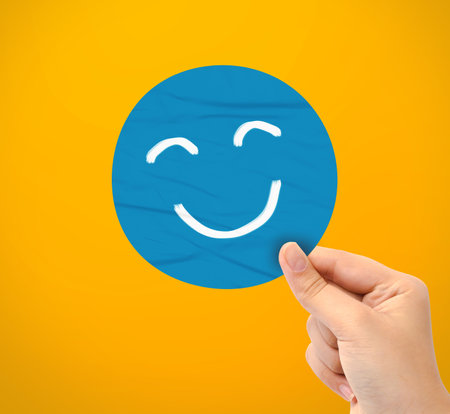 Hand holding blue happy smile face paper cut on yellow backgroundの写真素材
