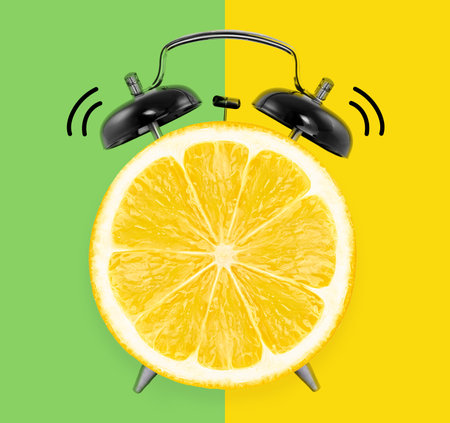 Flat lay creative art collage alarm clock with lemon slice on a yellow and green background, summer...