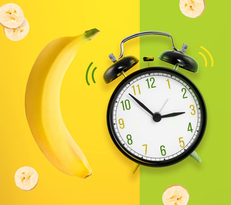 Alarm clock with yellow banana and banana slices on yellow and green backgroundの写真素材