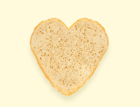 Abstract creative heart shaped cut-out from slice of white bread on light yellow background. Minimal flat lay. love food conceptの写真素材