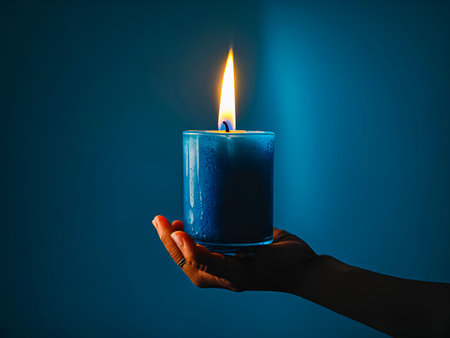 Hand Holding a Lit Candle, symbolizing light and warmth in darkness.の素材