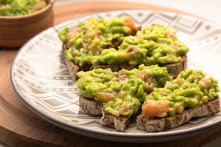 Appetizer of brown bread with avocado and salmon, on a plate and wooden background