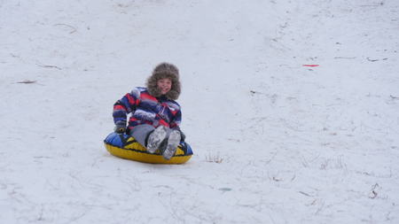 winter, leisure, sport, and people concept - happy teenage boy or young man sliding down on snow tube over mountain backgroundの写真素材