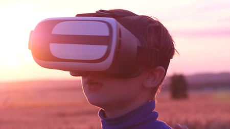 A boy stands in a wheat field at sunset in virtual glassesの写真素材