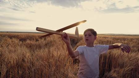 Happy child runs with a toy airplane on a sunset background over a wheat fieldの写真素材