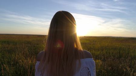 Romantic girl in a white dress walking in the golden wheat fields in the sunの写真素材