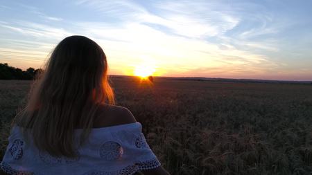 Romantic girl in a white dress walking in the golden wheat fields in the sunの写真素材
