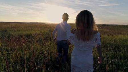 Young couple guy and girl running across the field towards the sunsetの写真素材